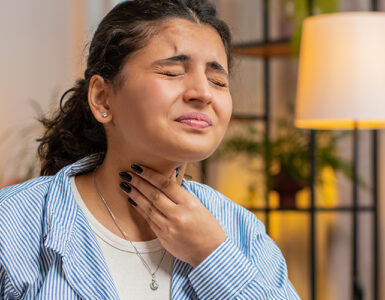 A woman holding her throat in pain while sitting at her desk at home.