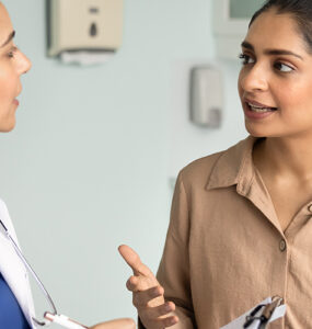 A woman in her 30s speaking to her female doctor in a medical office.