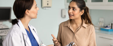 A woman in her 30s speaking to her female doctor in a medical office.