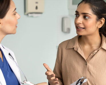 A woman in her 30s speaking to her female doctor in a medical office.