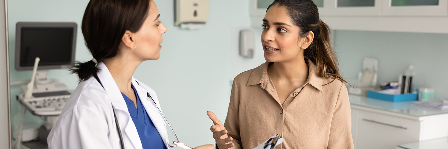 A woman in her 30s speaking to her female doctor in a medical office.