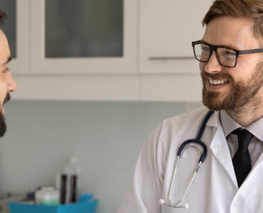 A male patient in his 40s speaking to a male doctor in his medical office, both smiling.