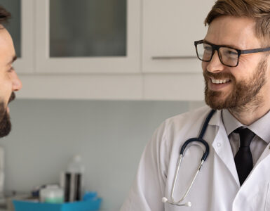 A male patient in his 40s speaking to a male doctor in his medical office, both smiling.