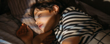 A teenage boy wearing a striped shirt, sleeping in his bed.