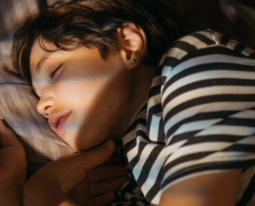A teenage boy wearing a striped shirt, sleeping in his bed.