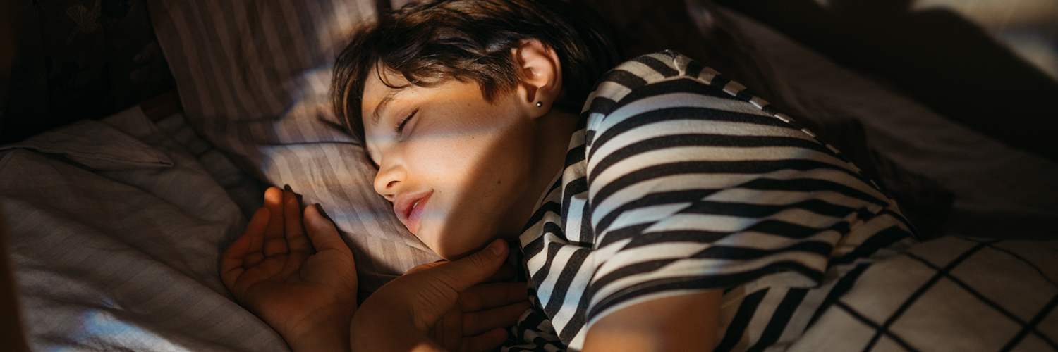 A teenage boy wearing a striped shirt, sleeping in his bed.