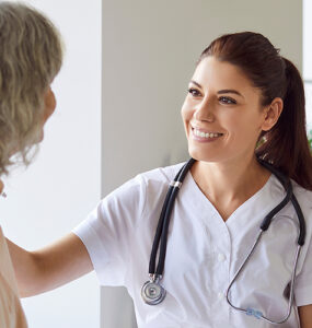 A female breast surgeon sitting with her patient, smiling at her while touching her shoulder.