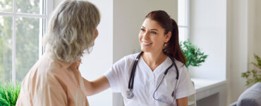 A female breast surgeon sitting with her patient, smiling at her while touching her shoulder.