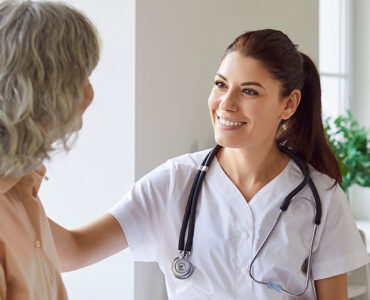 A female breast surgeon sitting with her patient, smiling at her while touching her shoulder.