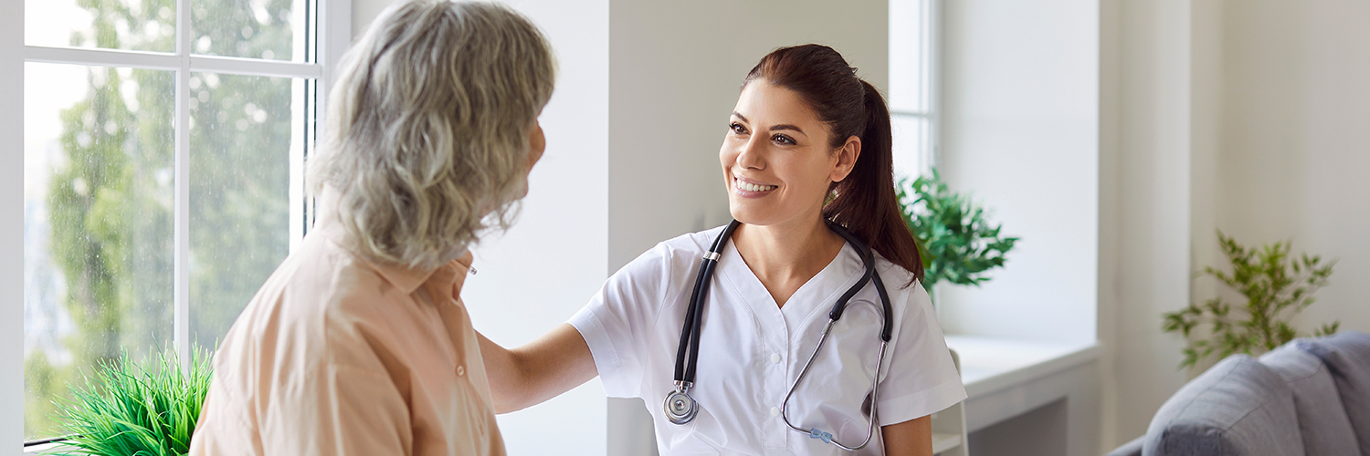 A female breast surgeon sitting with her patient, smiling at her while touching her shoulder.