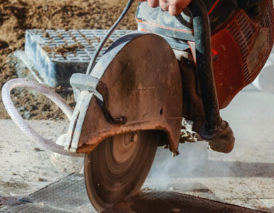 Construction worker using a circular saw to cut concrete, producing dust during outdoor construction work.