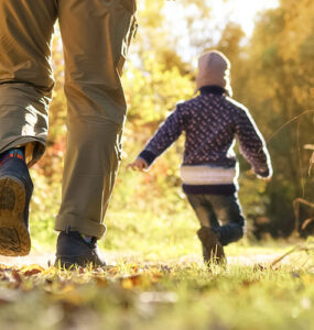 A father with two kids walking through a wooded area during the fall season.
