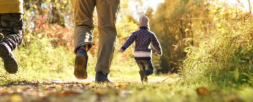 A father with two kids walking through a wooded area during the fall season.