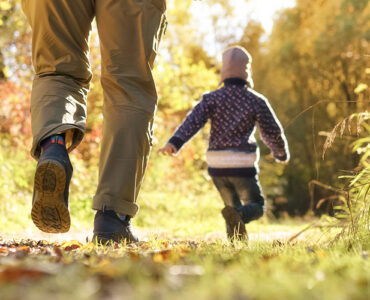A father with two kids walking through a wooded area during the fall season.