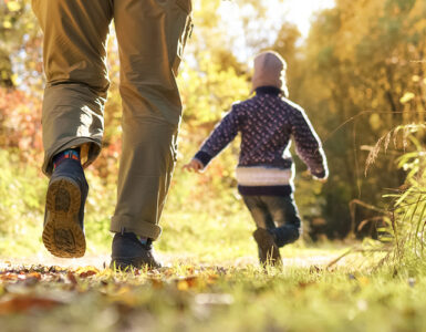 A father with two kids walking through a wooded area during the fall season.