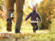 A father with two kids walking through a wooded area during the fall season.