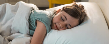 A young girl sleeping in her bed, wearing a green shirt with white bed sheets.