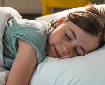 A young girl sleeping in her bed, wearing a green shirt with white bed sheets.