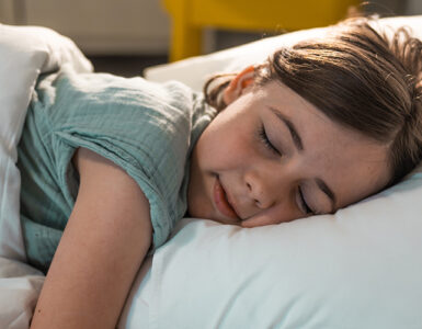 A young girl sleeping in her bed, wearing a green shirt with white bed sheets.
