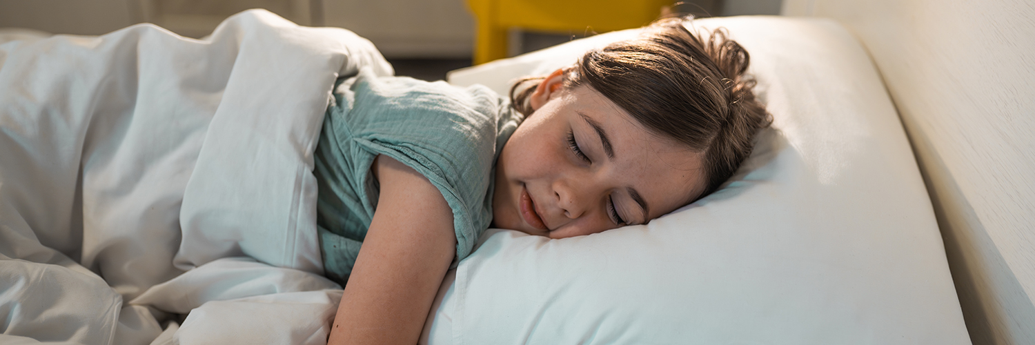 A young girl sleeping in her bed, wearing a green shirt with white bed sheets.