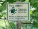 A sign outside in a wooded area warning hikers that ticks are present, with "Tick Alert!"