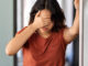 A young woman standing in her bathroom, covering her eyes because she's feeling dizzy.