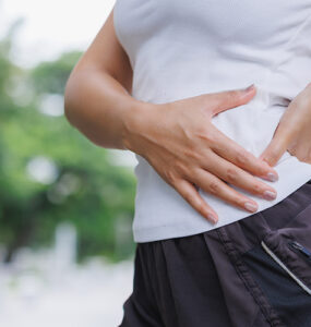 A young woman touching her upper hip in pain while running outside.