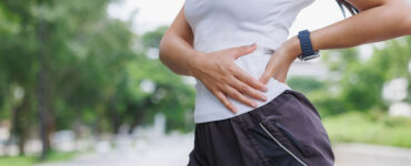 A young woman touching her upper hip in pain while running outside.