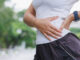 A young woman touching her upper hip in pain while running outside.