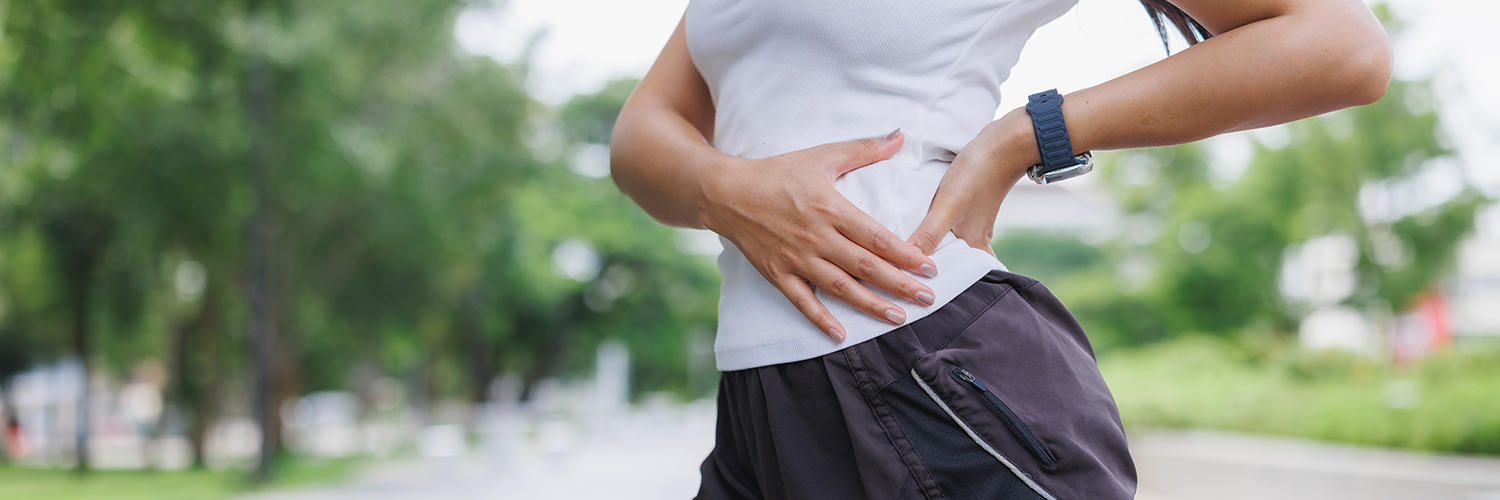 A young woman touching her upper hip in pain while running outside.