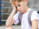 A young boy at school, sitting alone looking sad with his hand on his head.