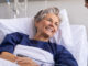 An older female patient sitting up in a hospital bed, smiling at a young man next to her.