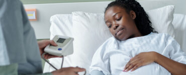 Black pregnant woman in hospital bed being checked by doctor
