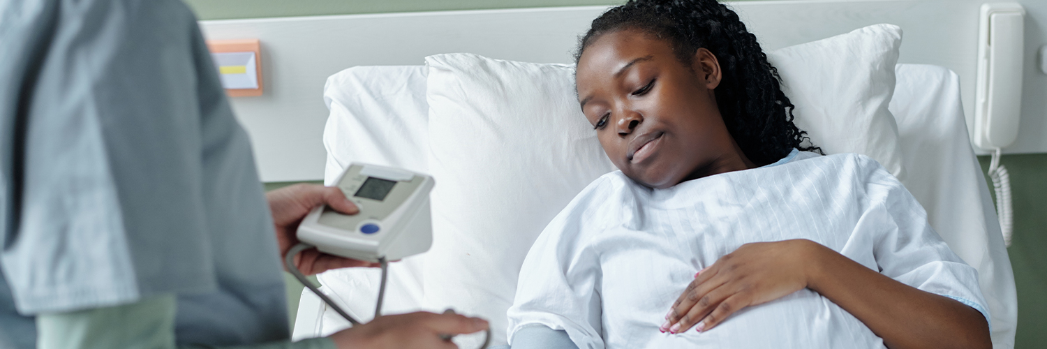 Black pregnant woman in hospital bed being checked by doctor