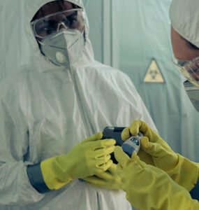 Two doctors standing together, wearing white protective clothing, with masks, gloves and goggles.
