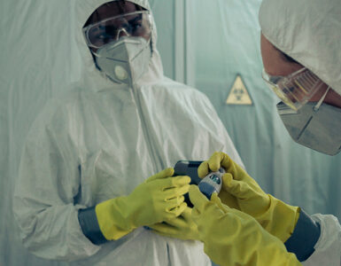 Two doctors standing together, wearing white protective clothing, with masks, gloves and goggles.