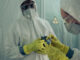 Two doctors standing together, wearing white protective clothing, with masks, gloves and goggles.