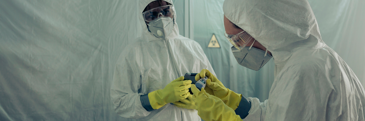 Two doctors standing together, wearing white protective clothing, with masks, gloves and goggles.