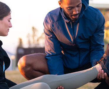 Sports therapist massaging the leg of a female athlete outdoors