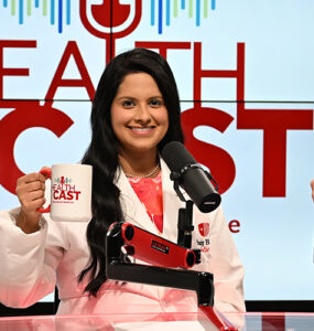 Three doctors in the Stony Brook Medicine studio holding their Healthcast-branded mugs in the air.