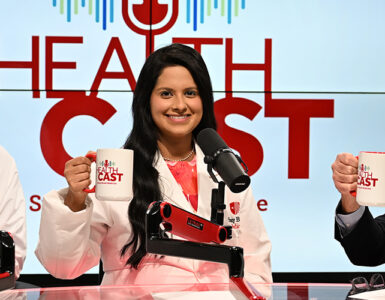 Three doctors in the Stony Brook Medicine studio holding their Healthcast-branded mugs in the air.