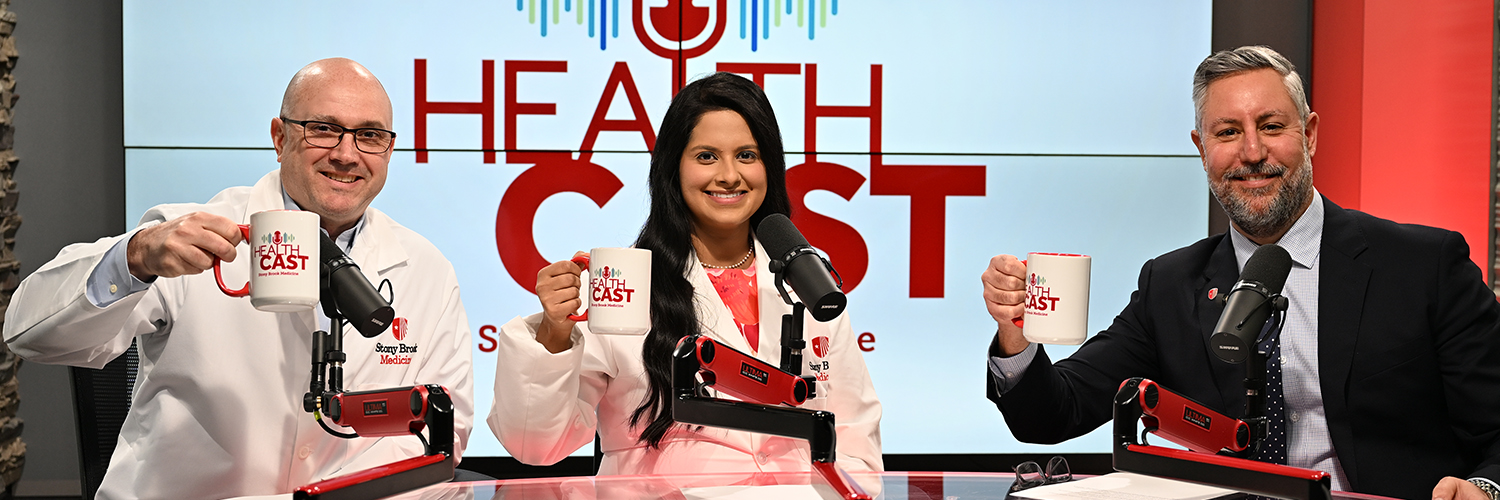 Three doctors in the Stony Brook Medicine studio holding their Healthcast-branded mugs in the air.