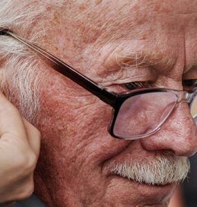 Elderly man being fitted for hearing aids and checked for dementia risk.
