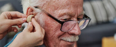 Elderly man being fitted for hearing aids and checked for dementia risk.