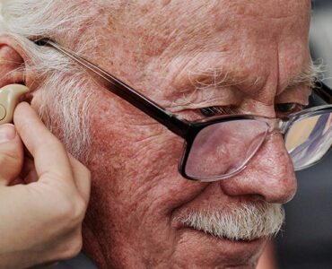 Elderly man being fitted for hearing aids and checked for dementia risk.