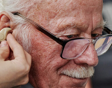 Elderly man being fitted for hearing aids and checked for dementia risk.