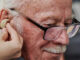 Elderly man being fitted for hearing aids and checked for dementia risk.