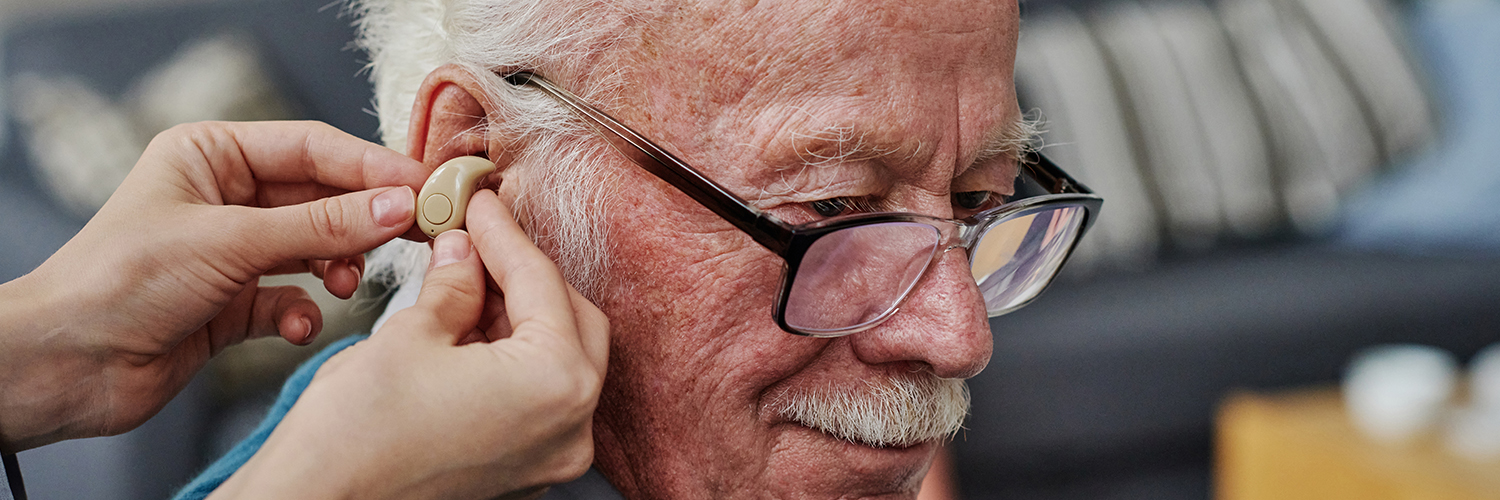 Elderly man being fitted for hearing aids and checked for dementia risk.