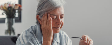 Elderly woman sits on a sofa at home suffering from a headache.