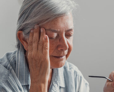 Elderly woman sits on a sofa at home suffering from a headache.